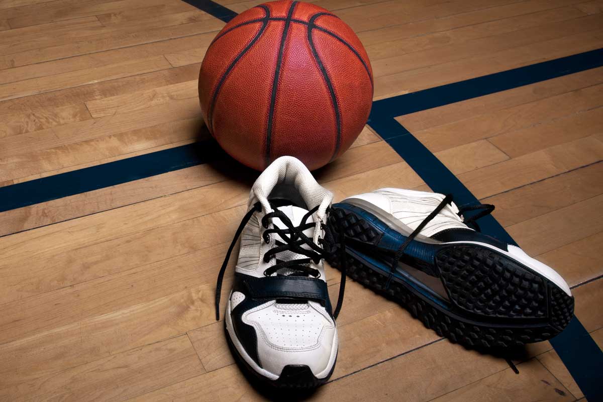 A basketball court floor with a ball and athletic shoes, Should Basketball Shoes Be Tight? [Important Fitting Tips!]