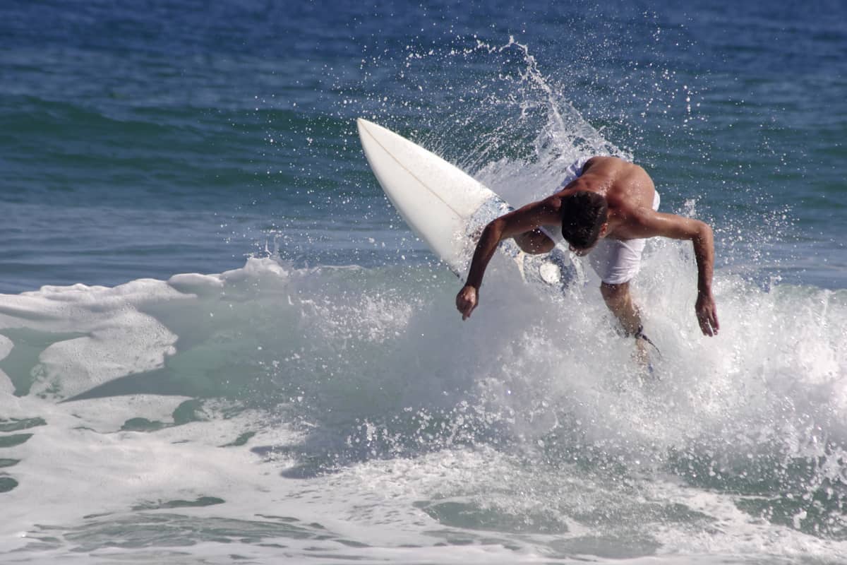 A surfer on a white surfboard riding rough waves