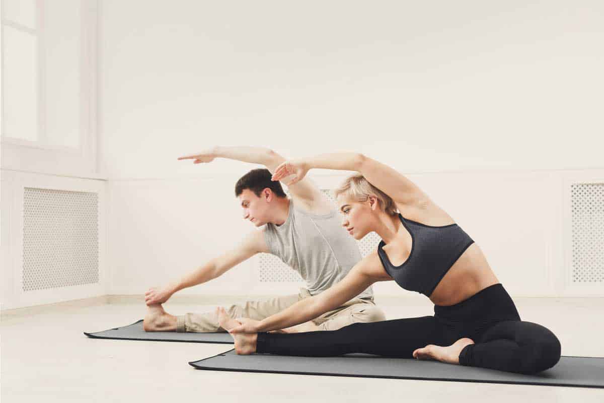 Fitness couple warmup stretching training, sitting on mat indoors. Young man and woman makes aerobics exercise, copy space