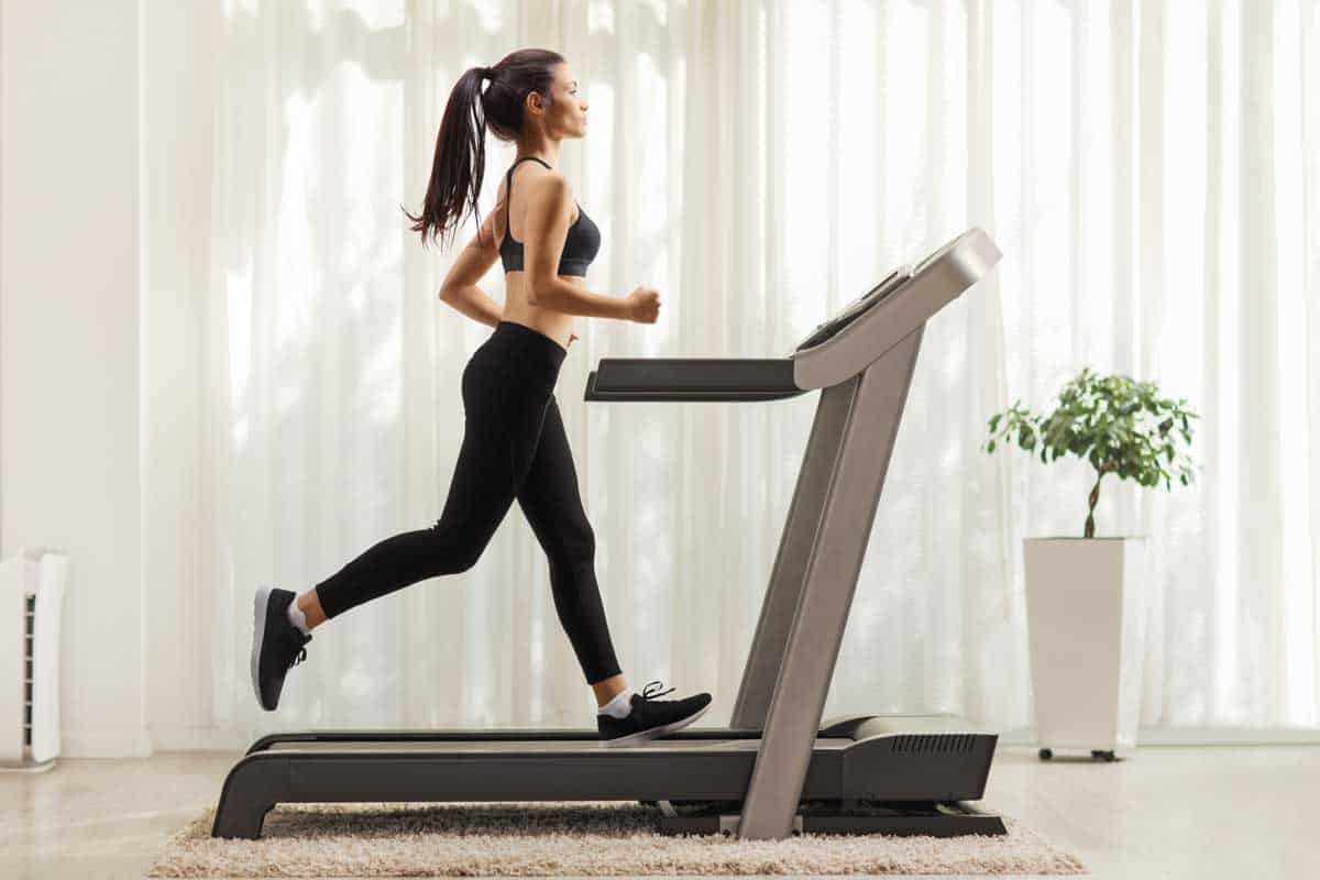 Full length profile shot of a young woman running on a treadmill indoors, How Long Does a Treadmill Last? (Leading Brands Explored)