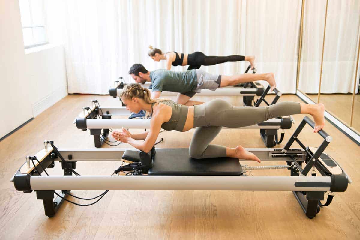Group of friends doing pilates kneeling glutes exercises on reformer beds in a gym in a health and fitness concept