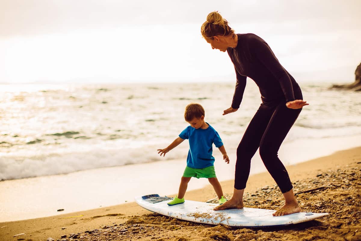 A mother teaching her son how to ride a surfboard
