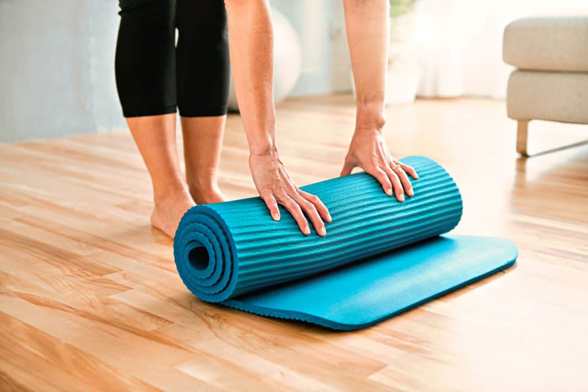 A woman unrolling her yoga mat on her living room before doing pilates