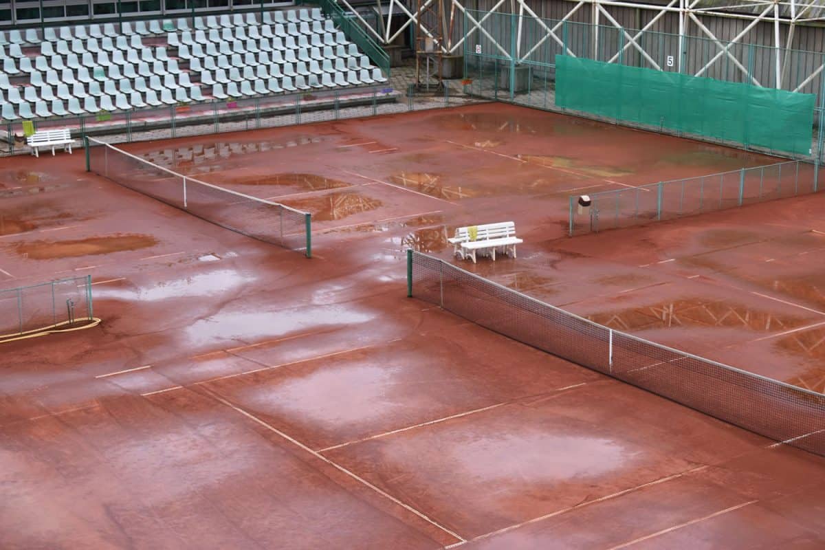 A tennis court with puddles of water due to unleveled surface