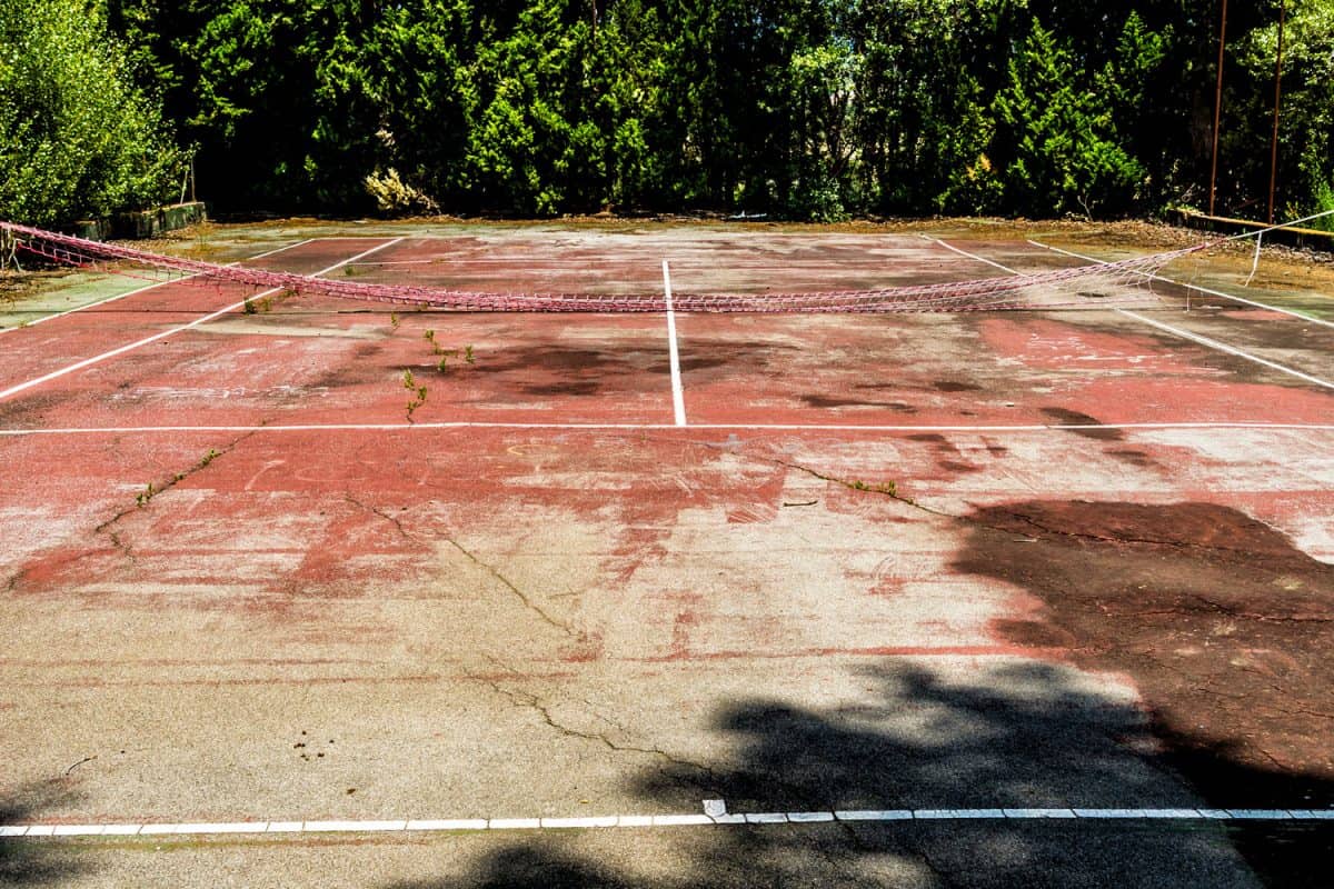 An unleveled tennis court with a deteriorating net