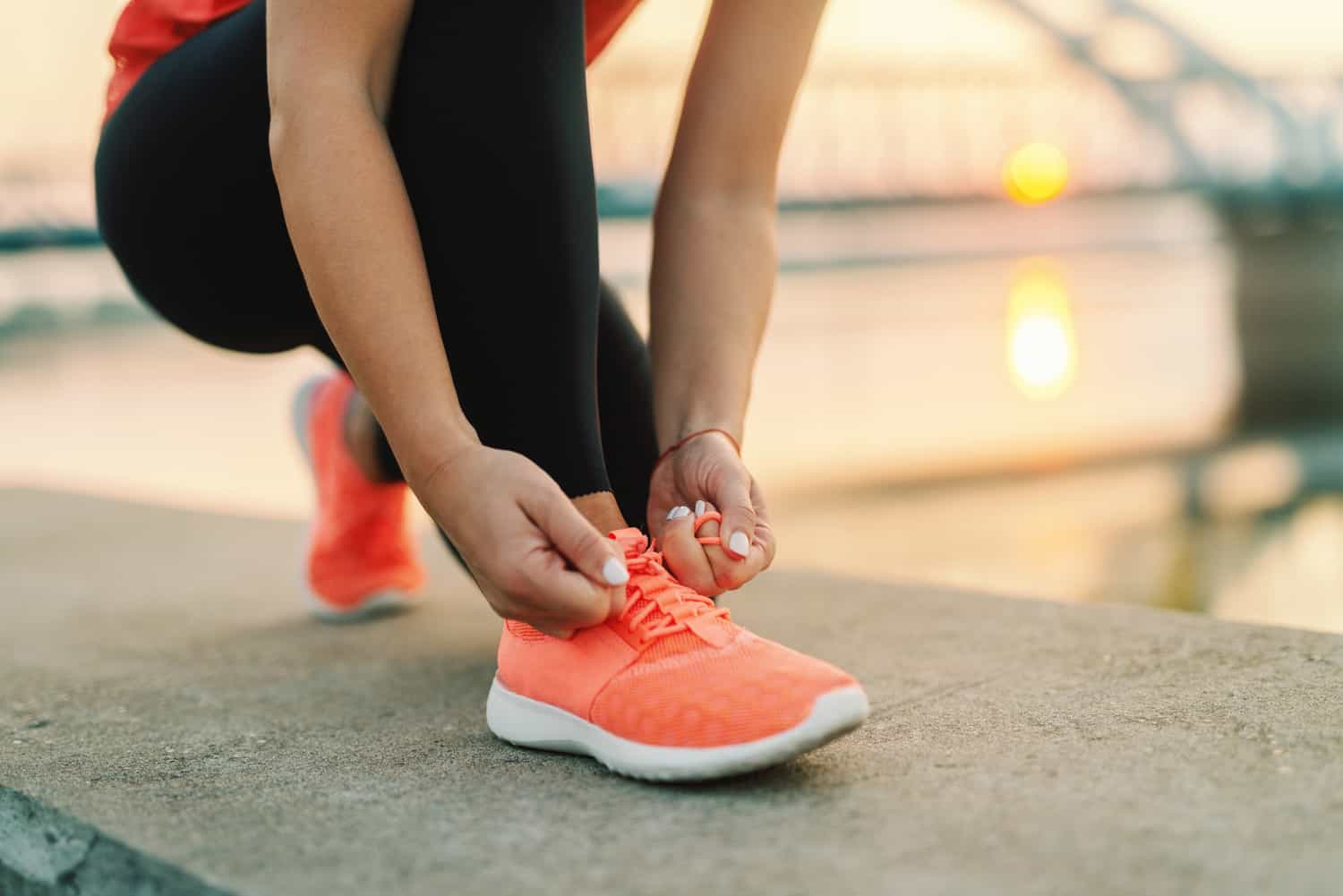 Close up of sporty woman tying shoelace while kneeling outdoor, In background bridge