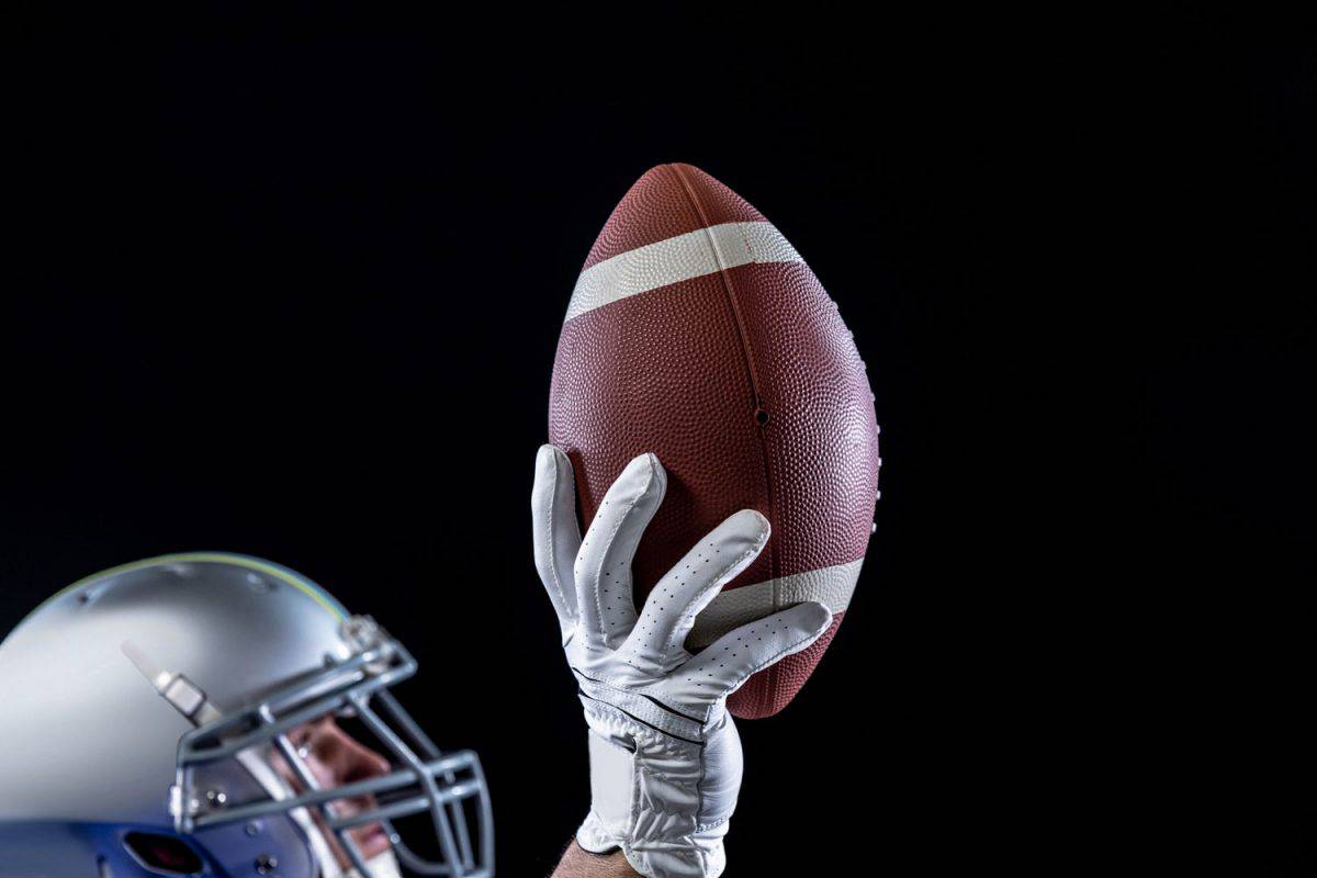 A selective focus photo of a football player catching a football on a black background