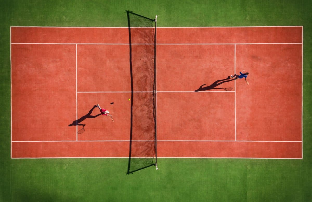 Drone view of tennis match from above with player's shadow