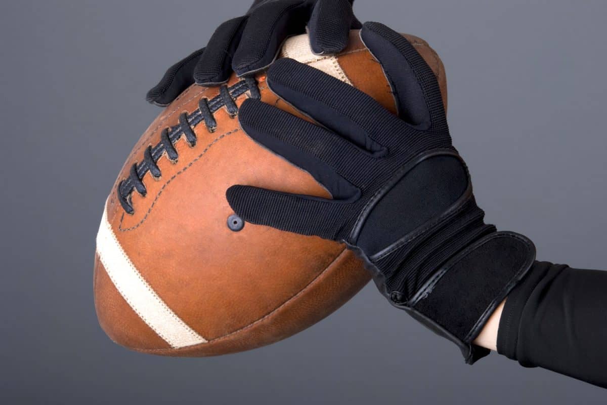 A football player wearing black colored gloves and holding a football tightly