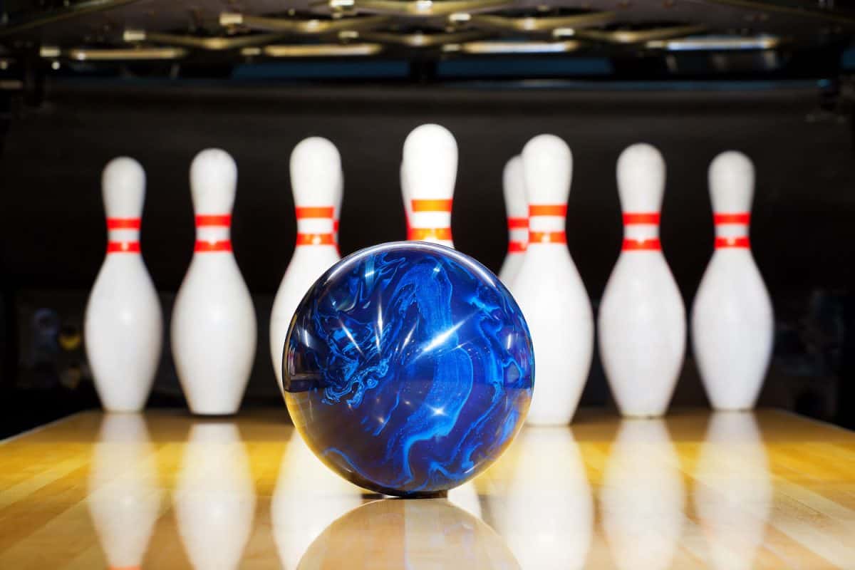 A blue resin bowling ball with bowling pins on the background