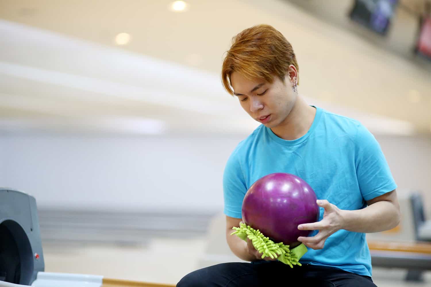 A male adult is wiping bowling ball with care.