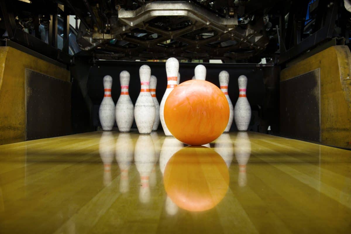 An orange bowling ball rolling to the bowling pins