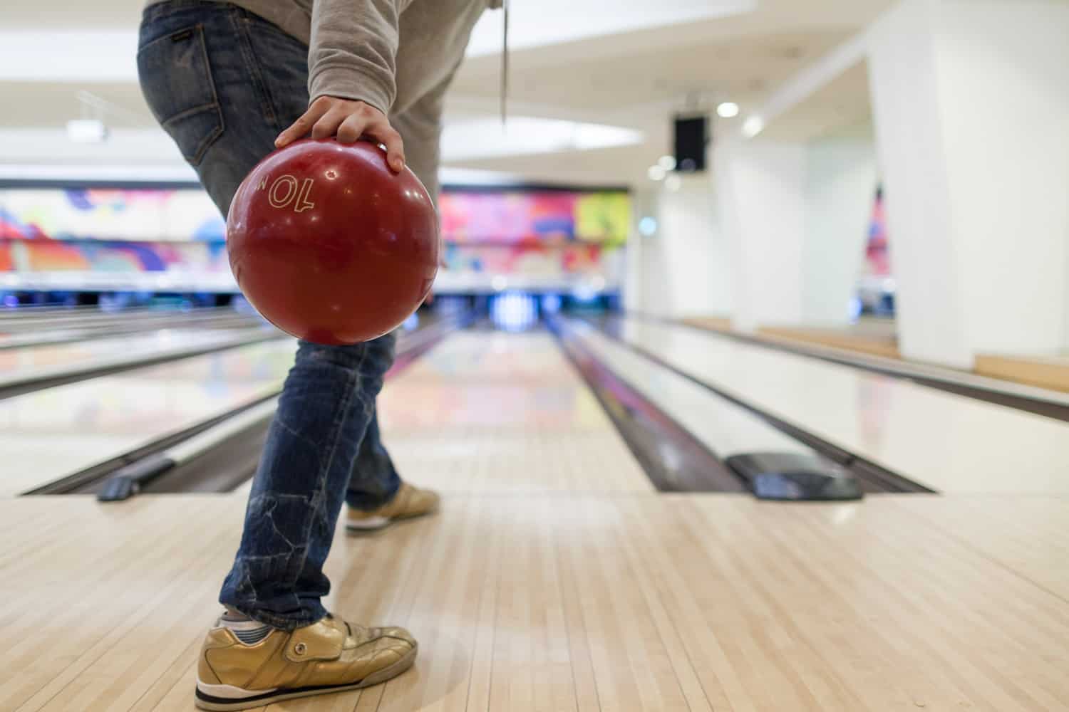An unrecognizable man is about to throw a bowling ball.