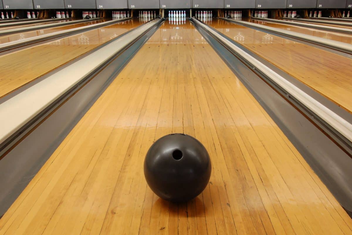 Black bowling ball rolling down the polished bowling lane