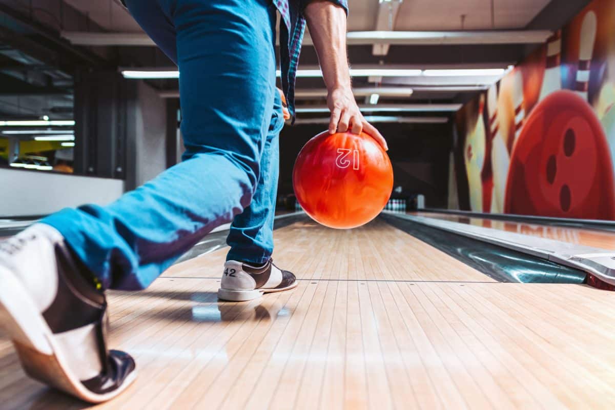 Bowling player getting to throw an orange bowling ball