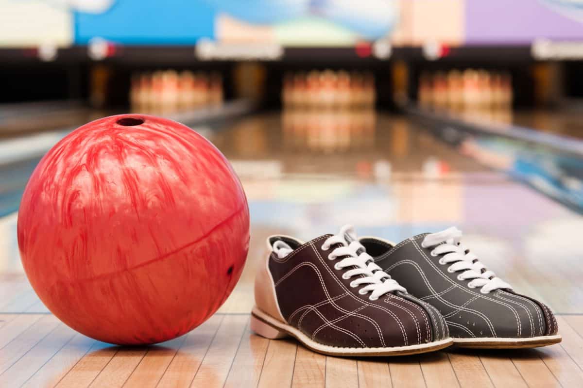 Bowling shoes with a red bowling ball on the side placed on the bowling alley