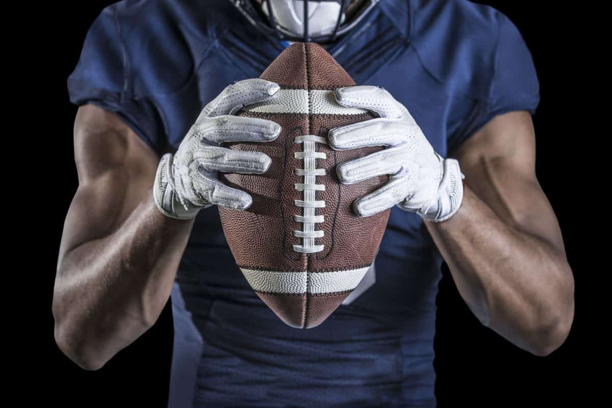 Football player wearing white football gloves holding the ball tightly