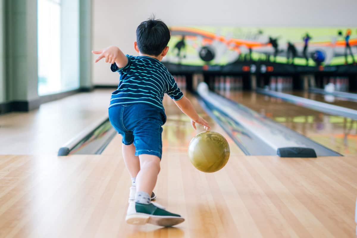 child throwing rolling bowling ball