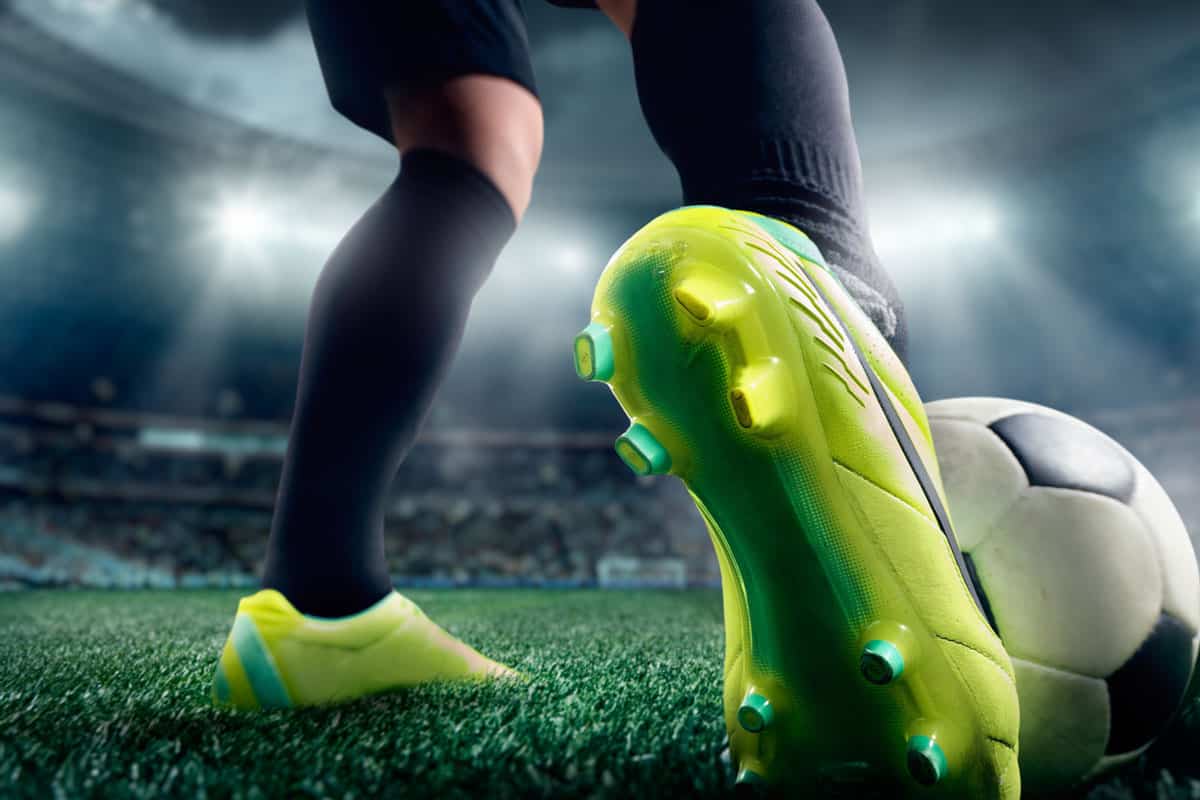 ground shot of a soccer player's foot wearing a lime-green shoe kicking a soccer ball