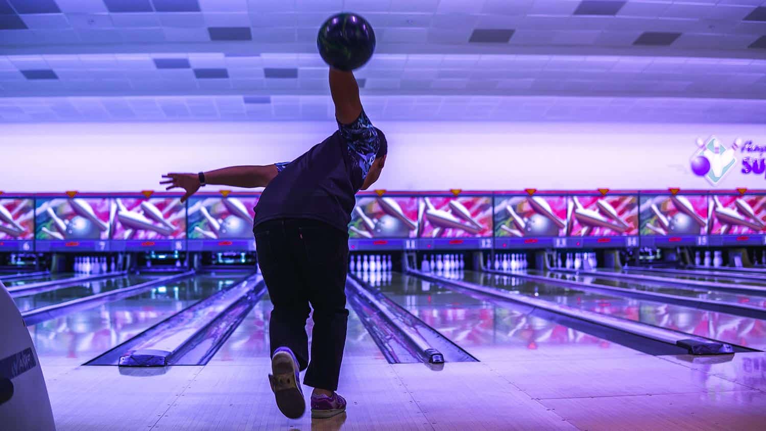 A adult boy lift up the bowling ball to strike into the tenpins bowling lanes